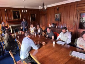 croup of academics and researchers meet around a wooden table in a wooden panelled college room